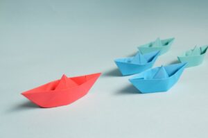 Red paper boat leading blue ones, symbolizing leadership and innovation