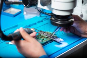Technician assembling smartphone circuit board under microscope in U.S. smartphone manufacturing lab