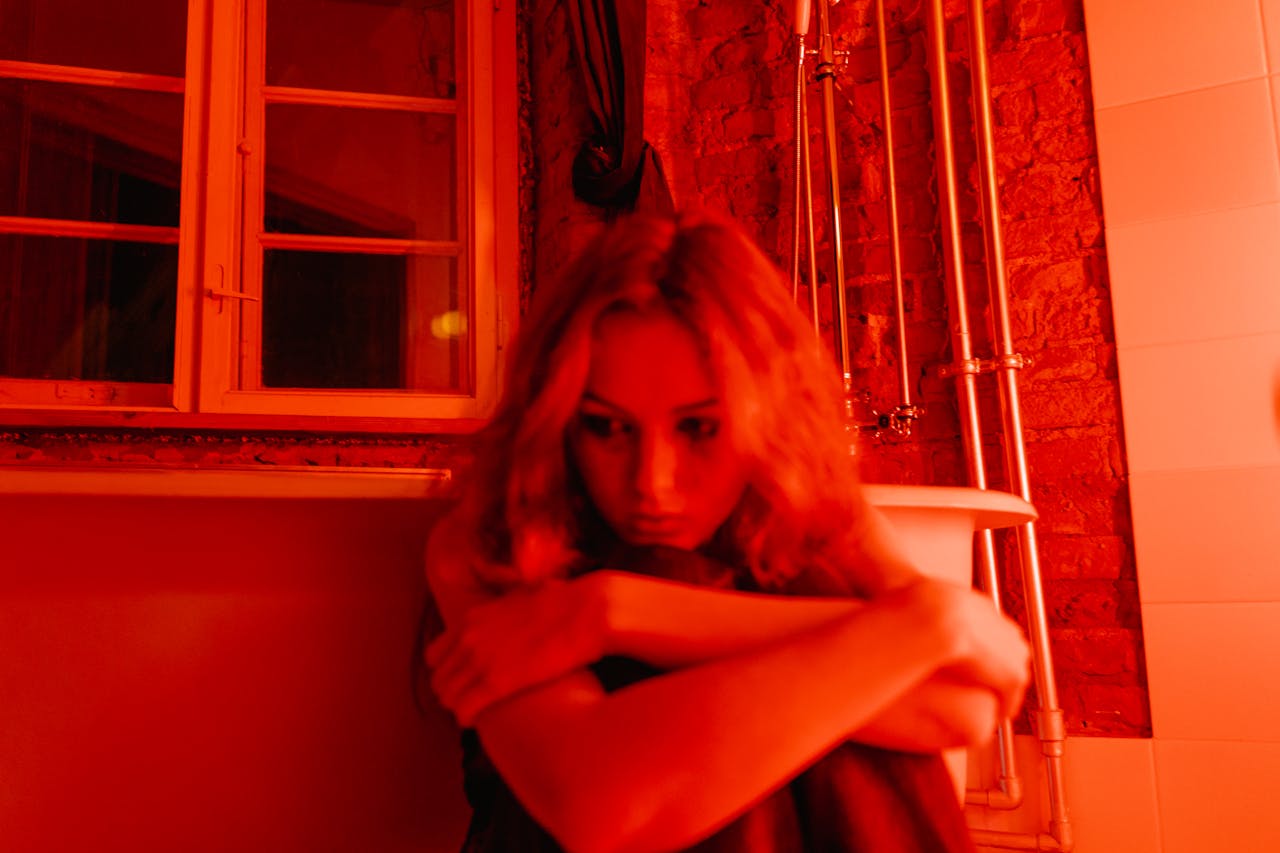 Person sitting alone in red-lit bathroom, symbolizing emotional isolation and loneliness
