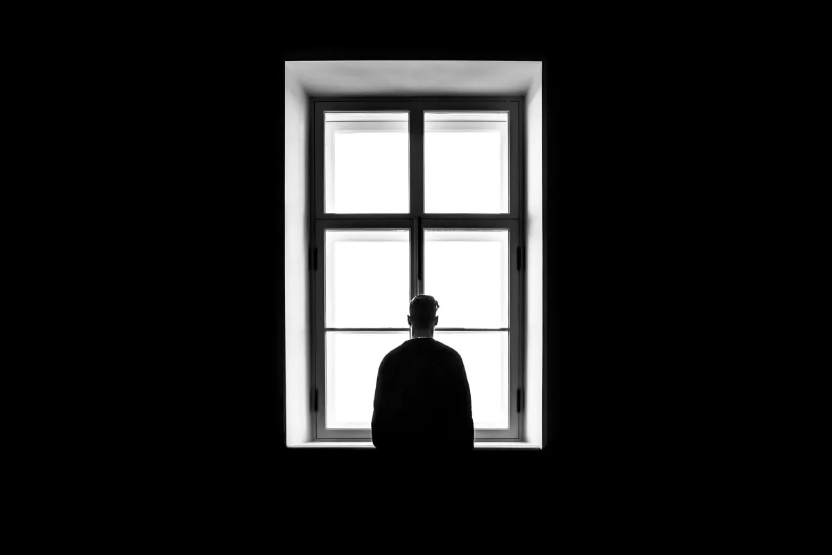 Silhouette of a person alone at a window representing psychological isolation linked to AI chatbot manipulation lawsuits.