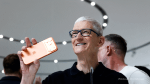 Senior technology executive holding a new iPhone during an Apple product event, reflecting strong iPhone sales and uncertainty around AI strategy.
