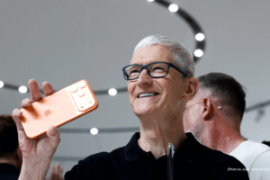 Senior technology executive holding a new iPhone during an Apple product event, reflecting strong iPhone sales and uncertainty around AI strategy.